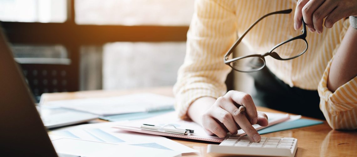 Close up Business woman using calculator and laptop for do math finance on wooden desk in office and business working background, tax, accounting, statistics and analytic research concept